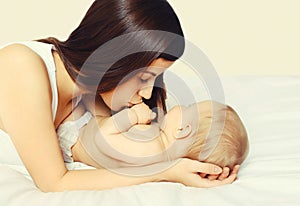 Portrait of happy young mother and cute baby lying on the bed at home together on white background