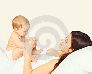 Portrait of happy young mother and cute baby lying on the bed at home together on white background