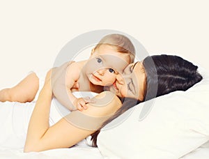 Portrait of happy young mother and cute baby lying on the bed at home together on white background