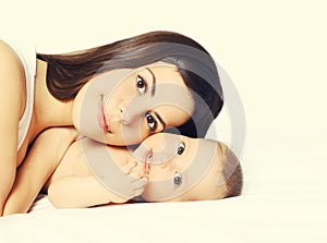 Portrait of happy young mother and cute baby lying on the bed at home together on white background