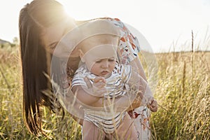Happy young mother with cute baby son joyful exploring the world on field at sunny day