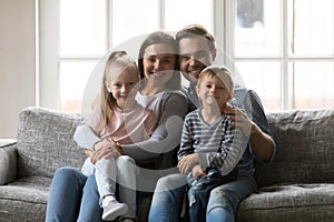 Portrait of happy young parents holding on laps little children.