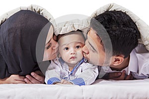 Young parents kissing their baby under blanket