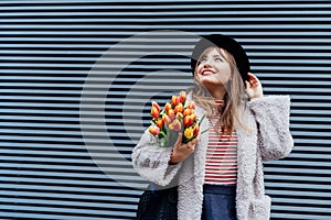Portrait of happy, young smiling fashion woman enjoying the moment, holding bunch of fresh tulip flowers on the gray