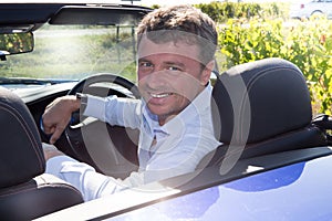 Portrait happy young smiling handsome man in blue shirt in new cabriolet car, relaxing, looking at camera