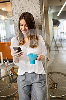 Portrait of a happy young success woman using smartphone and drinking coffee in break