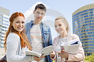 Portrait of happy young university students studying outdoors