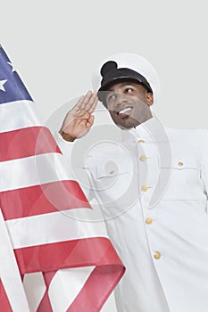 Portrait of a happy young US Navy officer saluting American flag over gray background