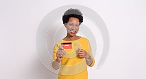 Portrait of happy young woman with afro hair showing credit card while standing on white background