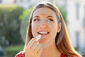 Portrait of a happy young woman applying lip balm in summer time outdoor