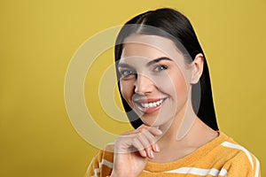 Portrait of happy young woman with beautiful black hair and charming smile on yellow background