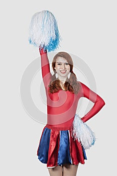 Portrait of happy young woman in cheer leader costume standing against gray background