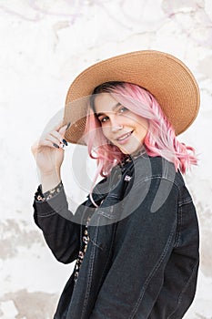 Portrait happy young woman with cute smile with glamour pink hair in stylish denim casual jacket near wall on street. Smiling girl