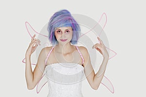 Portrait of happy young woman dressed as angel with dyed hair against gray background