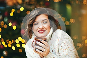 Portrait of happy young woman drinking hot chocolate next to Christmas treen