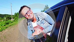 Portrait of happy young woman going on a road trip leaning out of window. Female enjoying travelling in a car