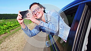 Portrait of happy young woman going on a road trip leaning out of window. Female enjoying travelling in a car