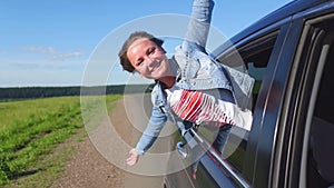 Portrait of happy young woman going on a road trip leaning out of window. Female enjoying travelling in a car