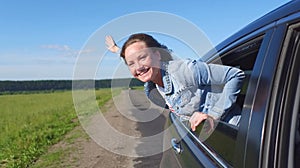 Portrait of happy young woman going on a road trip leaning out of window. Female enjoying travelling in a car