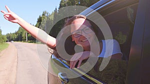 Portrait of happy young woman going on a road trip leaning out of window. Female enjoying travelling in a car
