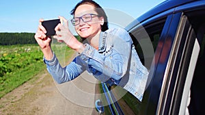 Portrait of happy young woman going on a road trip leaning out of window. Female enjoying travelling in a car