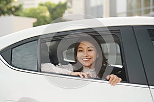 Portrait of happy young woman going on a road trip leaning out of window. Female enjoying travelling in a car with her boyfriend