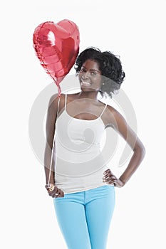 Portrait of happy young woman with heart shaped balloon standing over white background