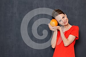 Portrait of happy young woman holding grapefruit near head