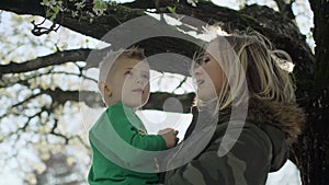 Portrait of happy young woman holding her baby son under tree at backyard 4k