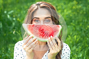 Portrait of happy young woman is holding slice of watermelon over green background
