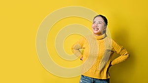 Portrait of happy young woman laughing against yellow wall. Photo of positive excited. person in sweater rejoices on yellow studio