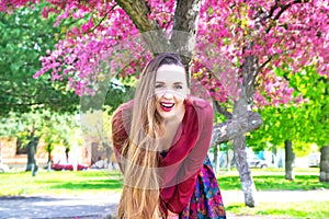 Portrait of happy young woman with long hair smiling on camera in front of Sakura