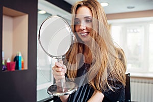 Portrait of happy young woman looking in the mirror sitting in a beauty salon
