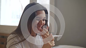 Portrait of happy young woman looking at pregnancy test. Girl smiling after the positive result of pregnancy test
