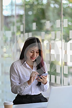 Happy young woman office worker sitting in office and using mobile phone.