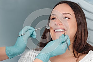 Portrait of happy young woman with open mouth sitting in dental chair, dentist holding in hands in blue gloves mouth mirror and