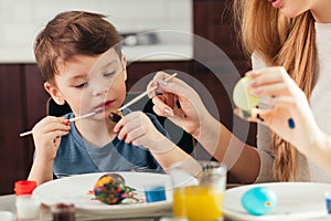 Portrait of happy young woman painting Easter eggs with her adorable little son