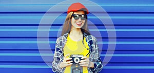 Portrait of happy young woman photographer taking picture on film camera wearing red baseball cap on blue background, banner blank