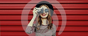 Portrait happy young woman photographer with vintage film camera on a red background