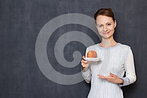 Portrait of happy young woman pointing at saucer with ripe peach