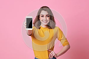 Portrait of happy young woman showing at blank screen mobile phone isolated over pink background