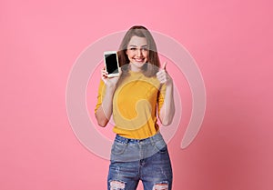 Portrait of happy young woman showing at blank screen mobile phone isolated over pink background