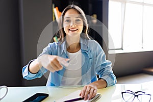 Portrait of happy young woman sitting looking at her laptop screen on video call, pointing on office background