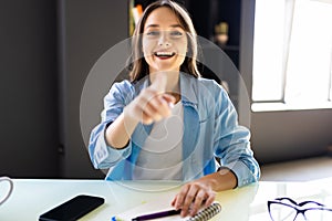 Portrait of happy young woman sitting looking at her laptop screen on video call, pointing on office background