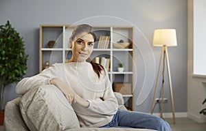 Portrait of a happy young woman sitting on the sofa at home and looking at the camera