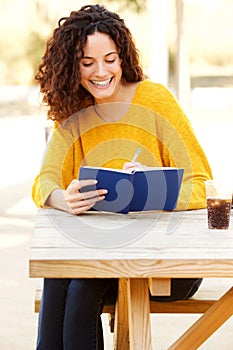 Happy young woman sitting at table writing notes in book