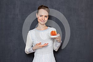 Portrait of happy young woman smiling, pointing at saucer with peach