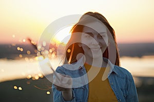 Portrait of happy young woman with sparkler in hand in summer evening