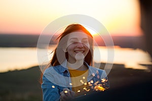 Portrait of happy young woman with sparkler in hand in summer evening