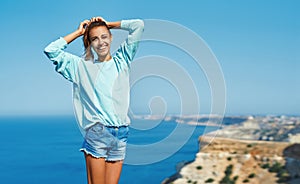 Portrait of happy young woman standing on cliff edge against amazing seascape and sky.